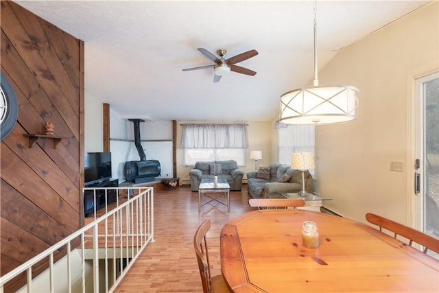 dining space with ceiling fan, wood-type flooring, a wood stove, and wooden walls