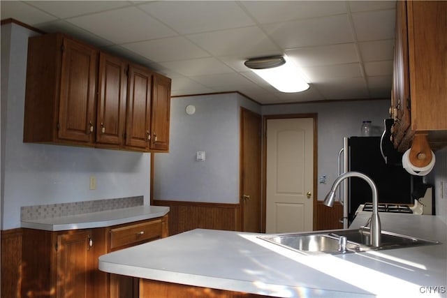 kitchen featuring fridge, a drop ceiling, wood walls, and sink