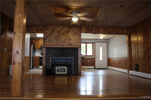 unfurnished living room with a wood stove, ceiling fan, light hardwood / wood-style flooring, and wood ceiling