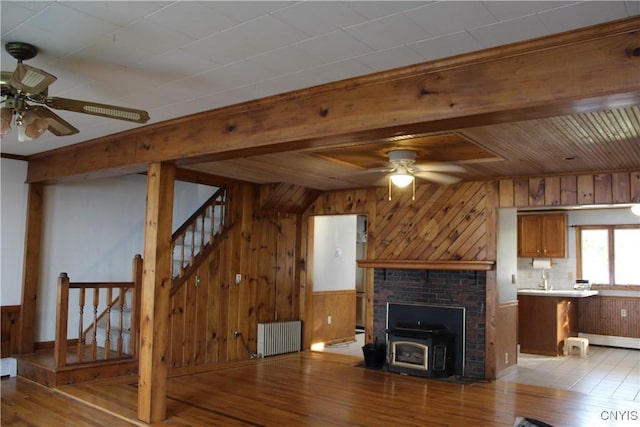 unfurnished living room featuring radiator heating unit, a wood stove, ceiling fan, and wood ceiling