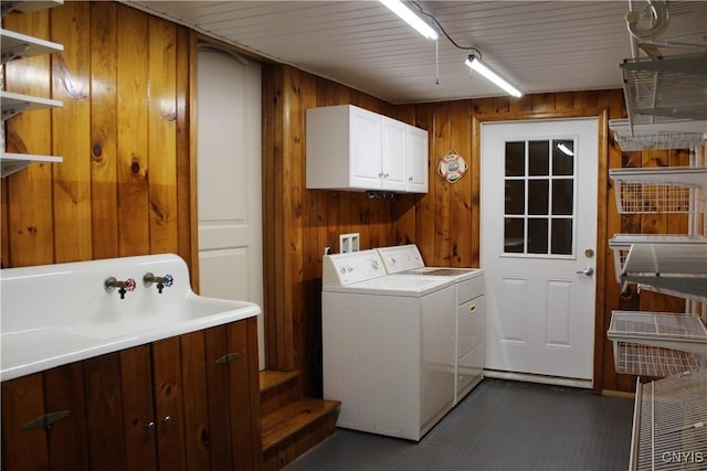 laundry area with wood walls, washer and clothes dryer, cabinets, and sink