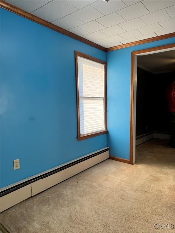 carpeted empty room with a baseboard heating unit and crown molding