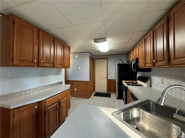 kitchen with white gas range, sink, a drop ceiling, backsplash, and wooden walls