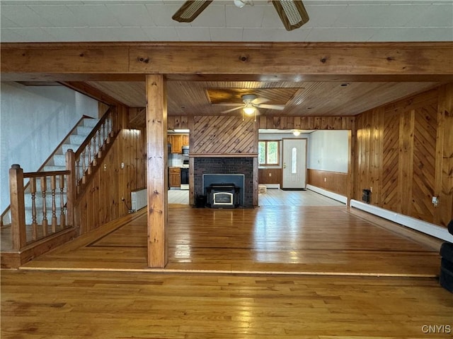 unfurnished living room featuring ceiling fan, wood-type flooring, a wood stove, and wooden walls