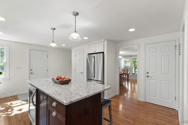 kitchen featuring stainless steel refrigerator, white cabinetry, dark brown cabinetry, a center island, and hardwood / wood-style floors