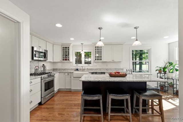 kitchen with white cabinetry, a center island, stainless steel appliances, pendant lighting, and light wood-type flooring