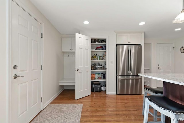 interior space featuring light stone countertops, hanging light fixtures, stainless steel fridge, white cabinets, and hardwood / wood-style flooring