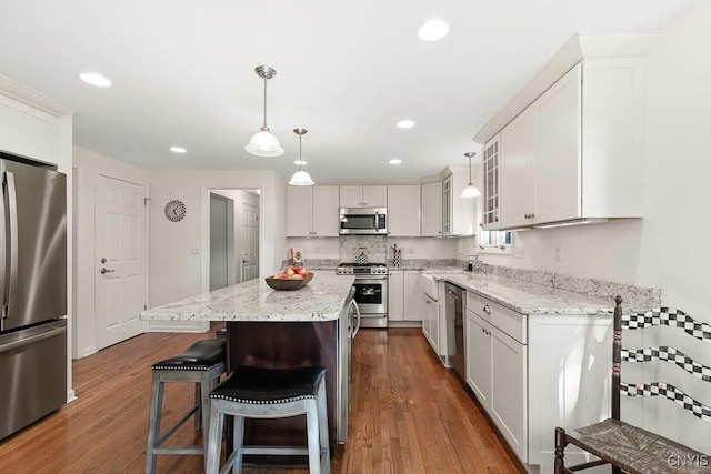 kitchen featuring white cabinets, appliances with stainless steel finishes, decorative light fixtures, and a kitchen island