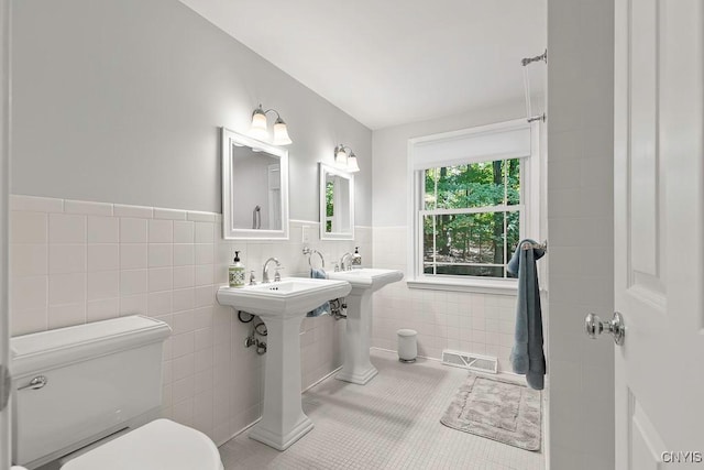 bathroom with tile patterned flooring, toilet, tile walls, and dual sinks