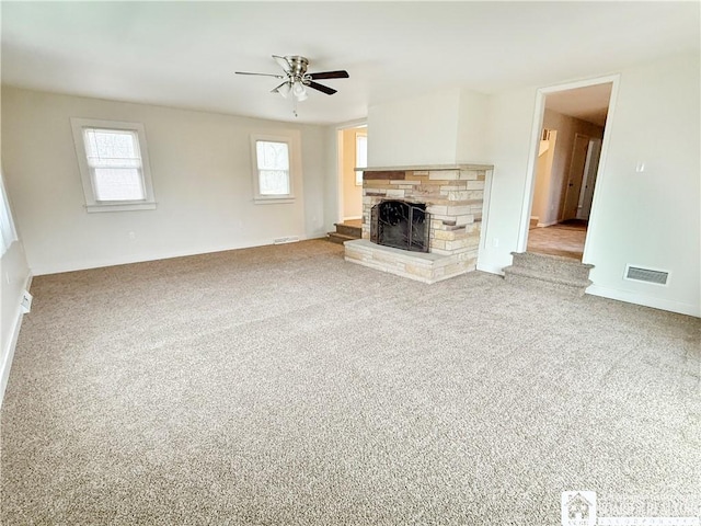 unfurnished living room featuring a stone fireplace, ceiling fan, and carpet floors