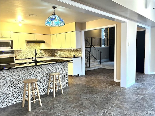 kitchen featuring sink, hanging light fixtures, stainless steel appliances, tasteful backsplash, and a kitchen bar