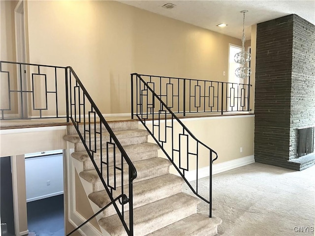 stairs with carpet floors, a fireplace, and an inviting chandelier