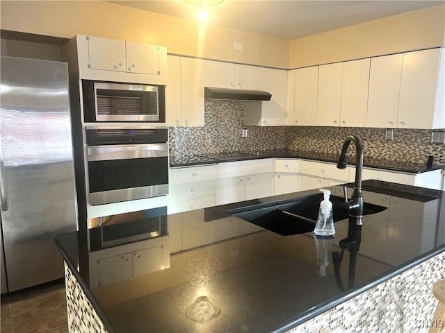 kitchen featuring white cabinets, backsplash, stainless steel appliances, and dark stone counters