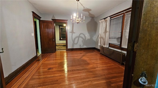 spare room with a chandelier, radiator heating unit, and hardwood / wood-style floors