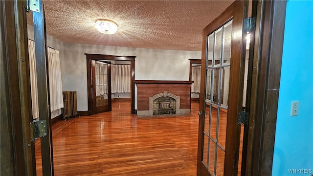 unfurnished living room with a fireplace, french doors, a textured ceiling, and hardwood / wood-style flooring