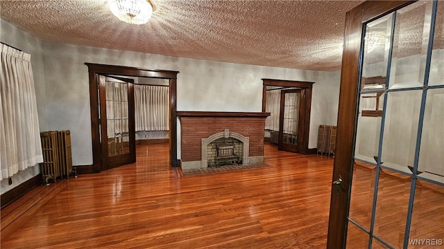 unfurnished living room with radiator, a brick fireplace, a notable chandelier, wood-type flooring, and a textured ceiling