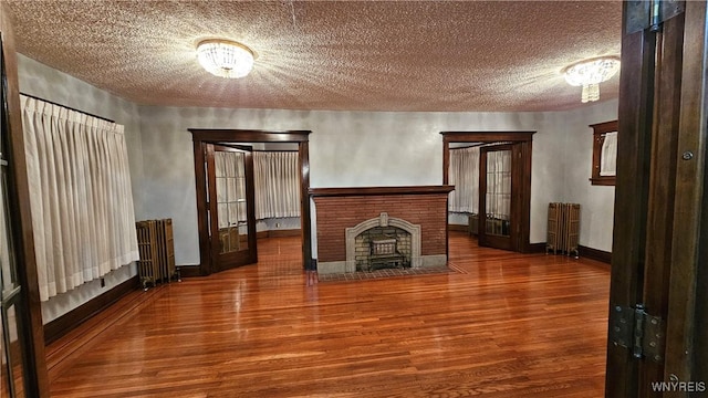 unfurnished living room with french doors, a brick fireplace, a textured ceiling, hardwood / wood-style floors, and radiator heating unit