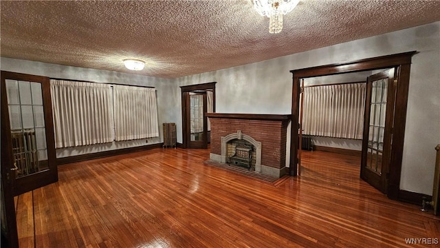 unfurnished living room featuring a fireplace, wood-type flooring, a textured ceiling, and french doors