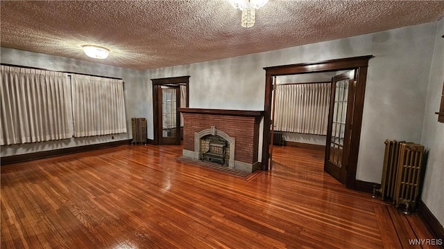 unfurnished living room with radiator, a fireplace, wood-type flooring, and a textured ceiling