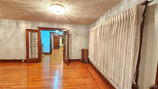 hall with radiator, french doors, a textured ceiling, and light hardwood / wood-style flooring