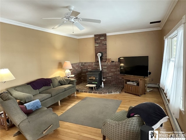 living room with ceiling fan, light wood-type flooring, a wood stove, and crown molding