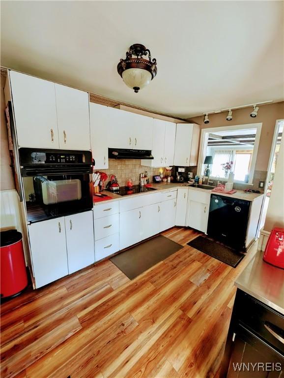 kitchen featuring decorative backsplash, white cabinets, light hardwood / wood-style flooring, and black appliances