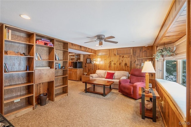 carpeted living room with ceiling fan and wooden walls