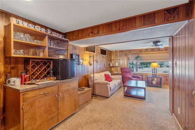 carpeted living room with bar area, ceiling fan, and wooden walls