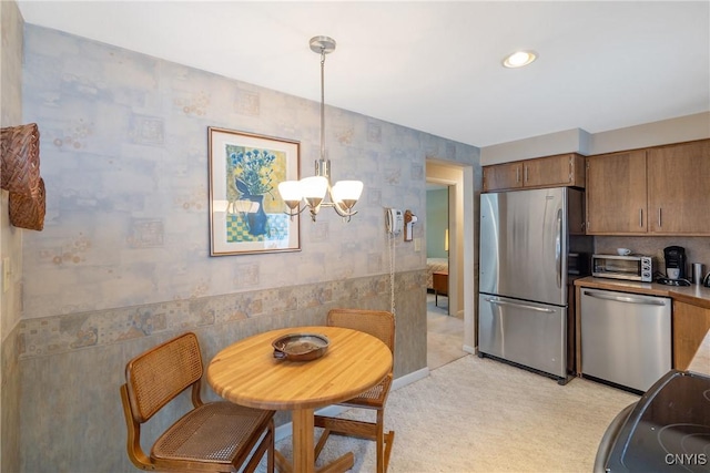 kitchen with light carpet, stainless steel appliances, hanging light fixtures, and a notable chandelier