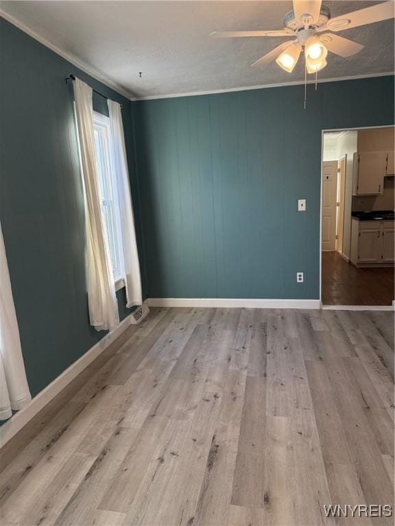 empty room featuring light wood-type flooring, ceiling fan, and crown molding