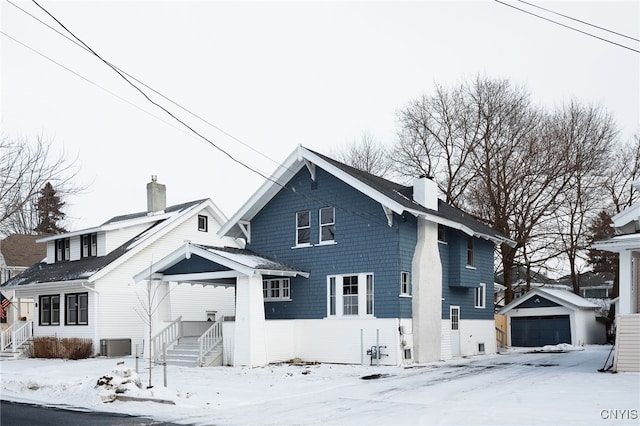 snow covered property featuring cooling unit, a garage, and an outbuilding