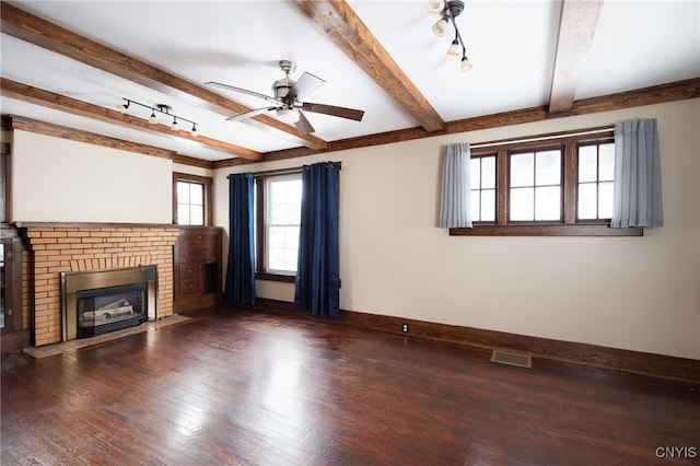 unfurnished living room featuring beam ceiling, ceiling fan, dark wood-type flooring, and a brick fireplace