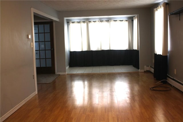 empty room featuring light hardwood / wood-style floors, a textured ceiling, and a baseboard heating unit