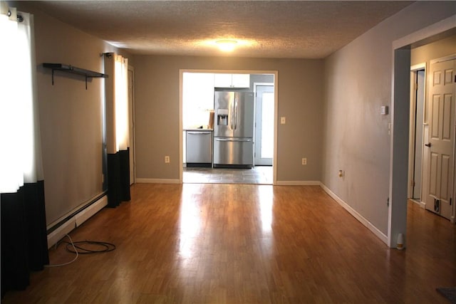 empty room with hardwood / wood-style floors, a textured ceiling, a baseboard radiator, and a healthy amount of sunlight