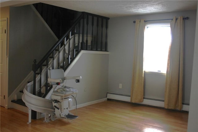 stairs with a wealth of natural light, a baseboard heating unit, and hardwood / wood-style flooring