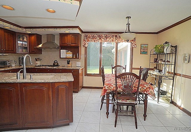 kitchen featuring sink, wall chimney exhaust hood, stainless steel gas cooktop, light stone counters, and decorative light fixtures