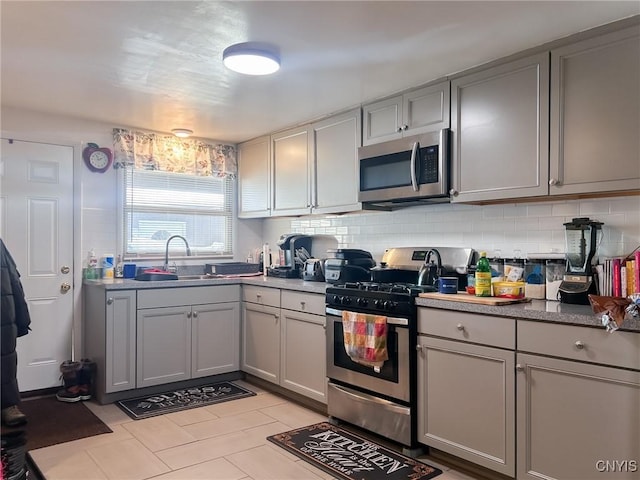 kitchen featuring sink, decorative backsplash, gray cabinets, light tile patterned floors, and stainless steel appliances