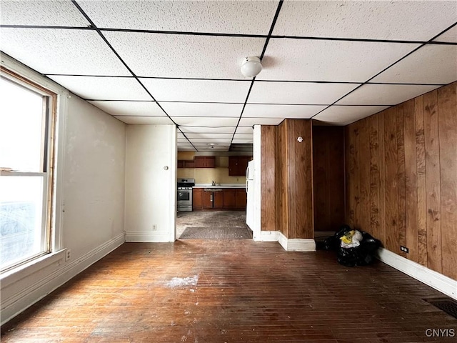 unfurnished living room with a paneled ceiling, hardwood / wood-style flooring, and wooden walls