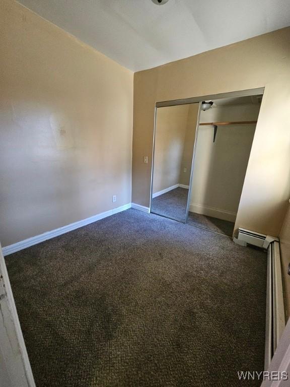 unfurnished bedroom featuring baseboard heating, a closet, and dark colored carpet