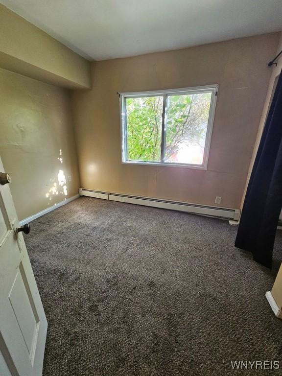 empty room featuring dark colored carpet and a baseboard heating unit