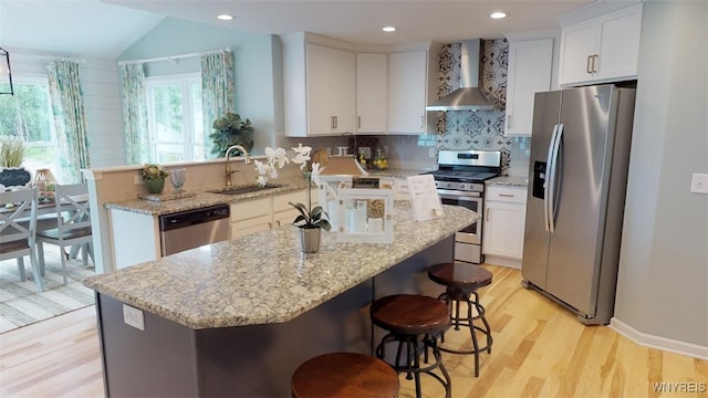 kitchen featuring appliances with stainless steel finishes, sink, wall chimney range hood, a center island, and white cabinetry