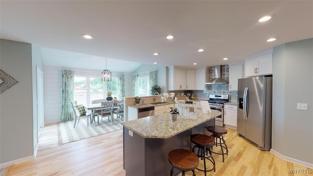 kitchen featuring appliances with stainless steel finishes, light stone counters, sink, wall chimney range hood, and white cabinets