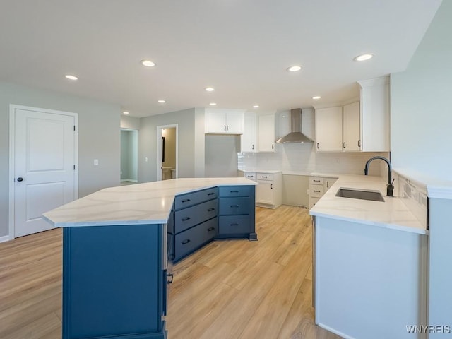 kitchen featuring light wood-style flooring, a sink, blue cabinetry, wall chimney exhaust hood, and white cabinets