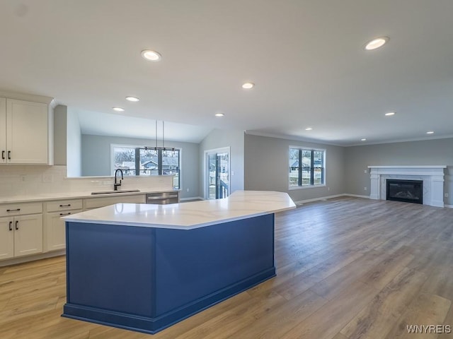 kitchen with a kitchen island, dishwasher, a glass covered fireplace, white cabinetry, and a sink