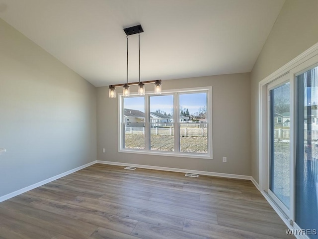 unfurnished dining area featuring lofted ceiling, wood finished floors, baseboards, and visible vents