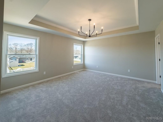 carpeted spare room featuring a chandelier, a raised ceiling, baseboards, and ornamental molding