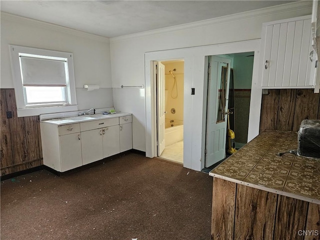 kitchen with white cabinets, wooden walls, and ornamental molding