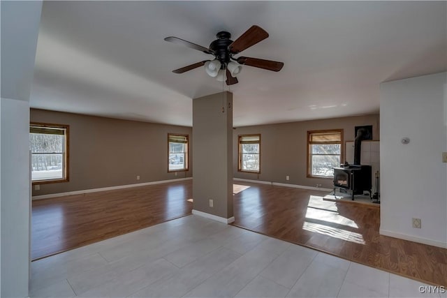 unfurnished living room featuring a wood stove, ceiling fan, and light wood-type flooring