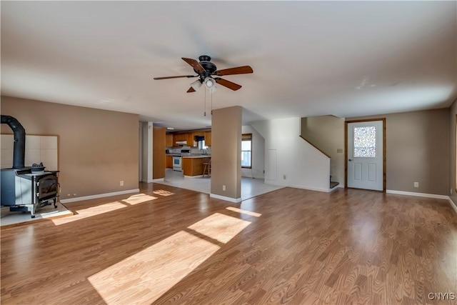 unfurnished living room with a wood stove, light hardwood / wood-style flooring, and ceiling fan