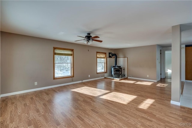 unfurnished living room with ceiling fan, a wood stove, and light hardwood / wood-style flooring